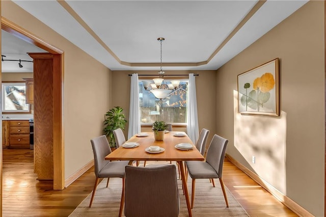 dining room featuring a raised ceiling, light hardwood / wood-style floors, and a notable chandelier