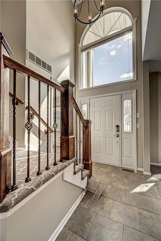 foyer entrance with baseboards, stairway, an inviting chandelier, a high ceiling, and stone tile flooring