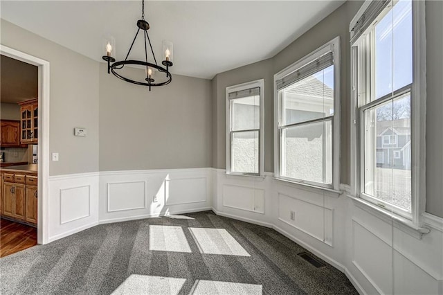 unfurnished dining area featuring a chandelier, wainscoting, dark carpet, and visible vents