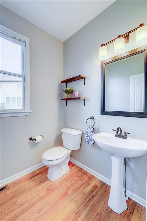 bathroom with toilet, a sink, wood finished floors, visible vents, and baseboards