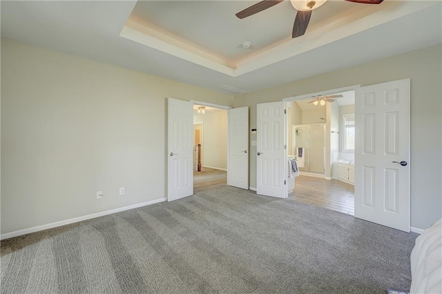 unfurnished bedroom featuring ceiling fan, connected bathroom, light colored carpet, baseboards, and a raised ceiling