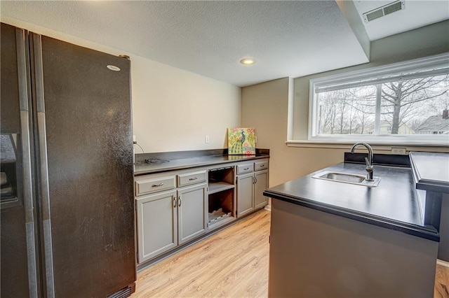 kitchen featuring a textured ceiling, a sink, visible vents, light wood-style floors, and dark countertops