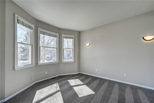 unfurnished room with dark carpet, visible vents, and baseboards