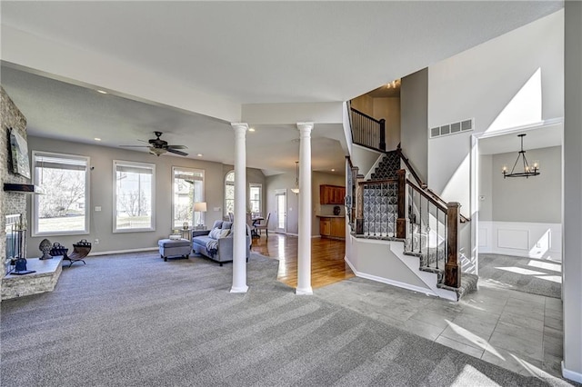 unfurnished living room featuring carpet floors, stairs, visible vents, ornate columns, and ceiling fan with notable chandelier