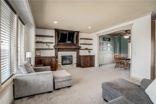 living room featuring a stone fireplace, a decorative wall, carpet flooring, and ornamental molding