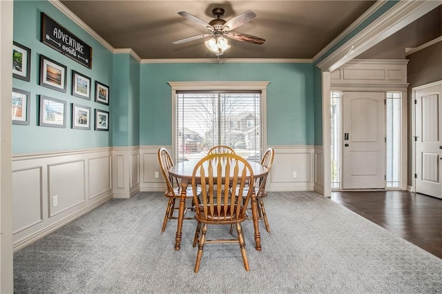 dining area featuring carpet flooring, wainscoting, ceiling fan, and ornamental molding