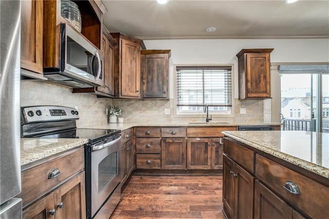 kitchen with tasteful backsplash, dark wood-type flooring, light stone countertops, appliances with stainless steel finishes, and a sink