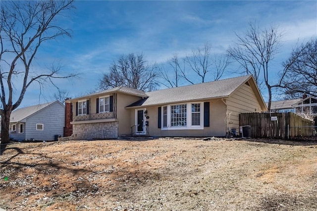 tri-level home with central AC unit, fence, and stucco siding