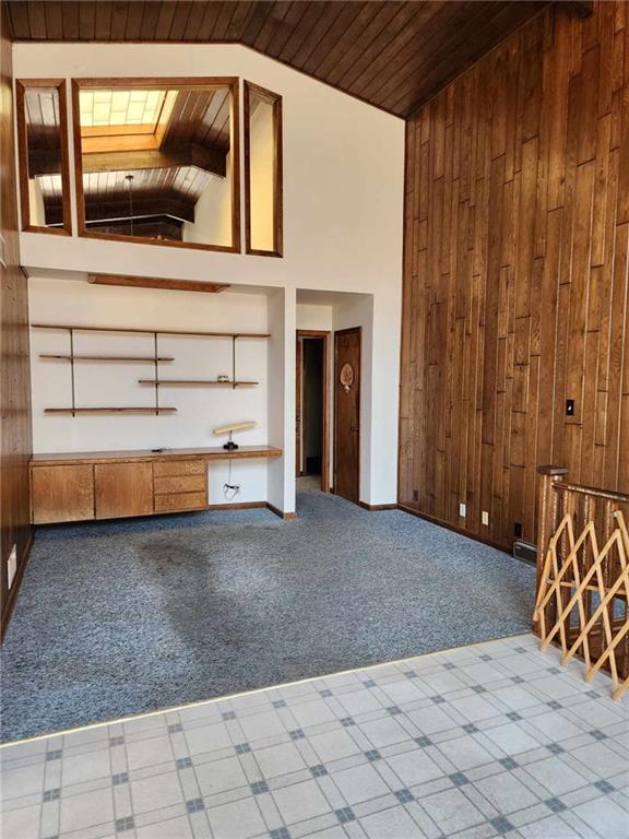 11425 45th Hwy N, Platte City, MO 64079 - unfurnished living room with wood ceiling, wood walls, carpet flooring, a skylight, and high vaulted ceiling