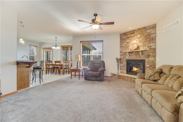 living area with visible vents, baseboards, a fireplace, carpet flooring, and ceiling fan with notable chandelier