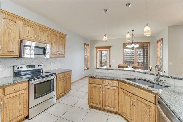 kitchen featuring light stone counters, an inviting chandelier, a sink, stainless steel appliances, and backsplash