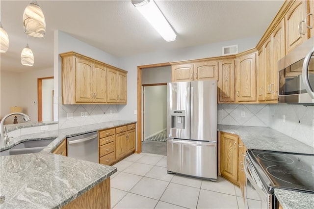 kitchen with light tile patterned floors, light stone counters, a sink, appliances with stainless steel finishes, and backsplash