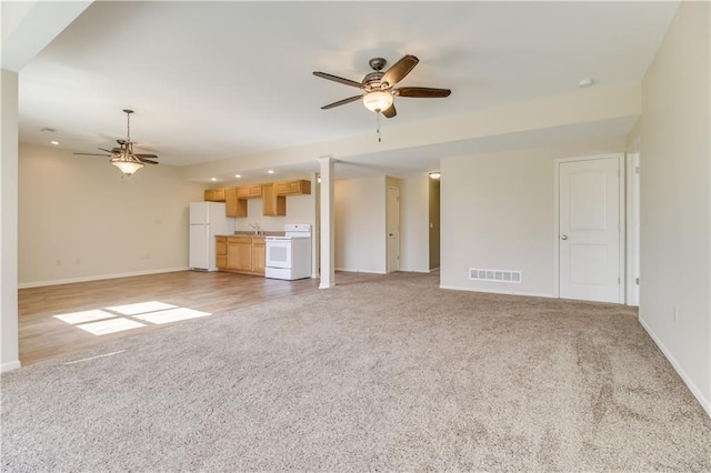 unfurnished living room with visible vents, a ceiling fan, a sink, baseboards, and light colored carpet