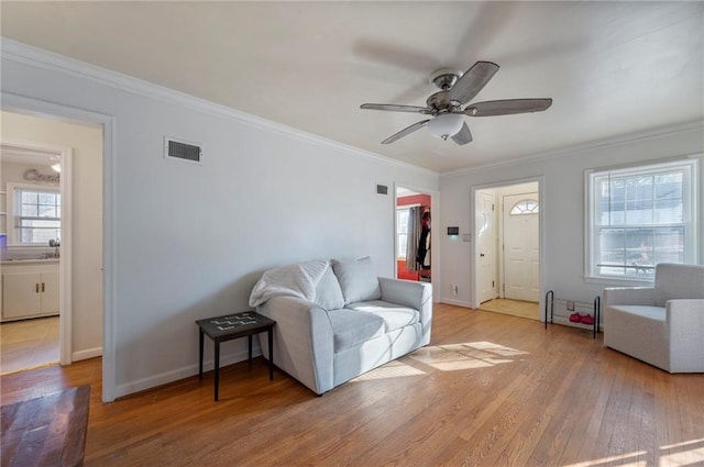 living room featuring baseboards, light wood finished floors, visible vents, and crown molding