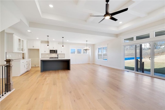 kitchen with hanging light fixtures, a kitchen island with sink, white cabinets, and light hardwood / wood-style floors