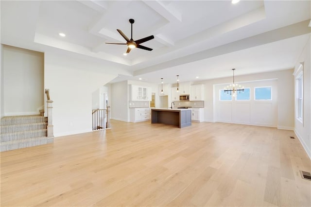 unfurnished living room featuring beam ceiling, coffered ceiling, ceiling fan with notable chandelier, and light wood-type flooring