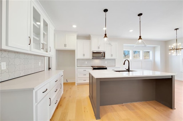 kitchen with sink, white cabinetry, an island with sink, pendant lighting, and light hardwood / wood-style floors