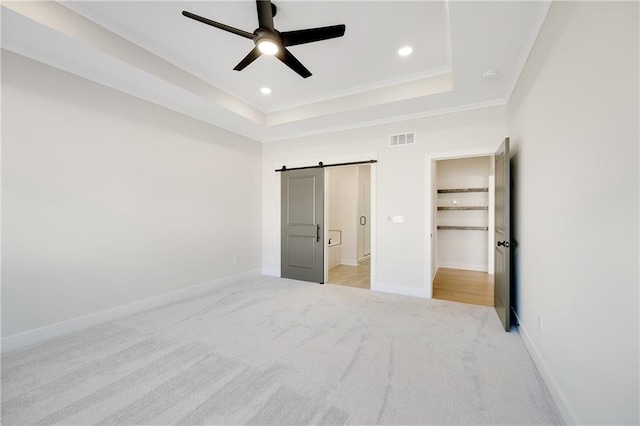 unfurnished bedroom featuring ceiling fan, a raised ceiling, crown molding, a barn door, and light carpet