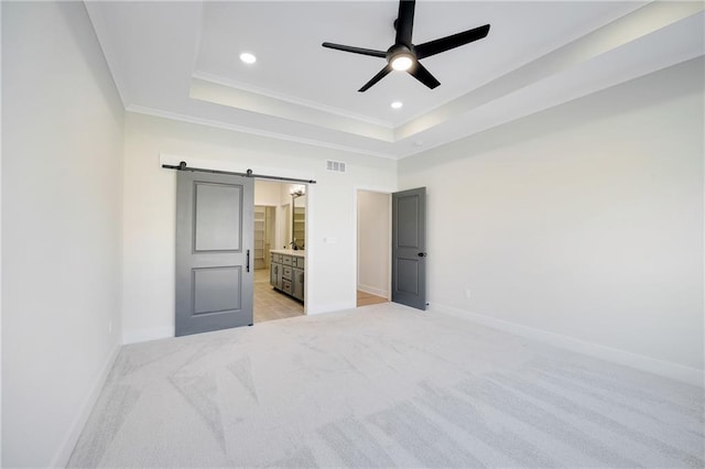 unfurnished bedroom featuring a raised ceiling, a barn door, light colored carpet, and connected bathroom