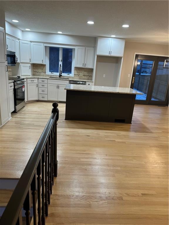 kitchen featuring white cabinets, light wood-type flooring, appliances with stainless steel finishes, and light stone countertops