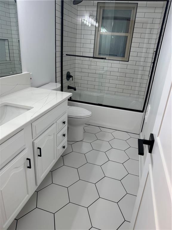 full bathroom featuring toilet, shower / bath combination with glass door, and vanity