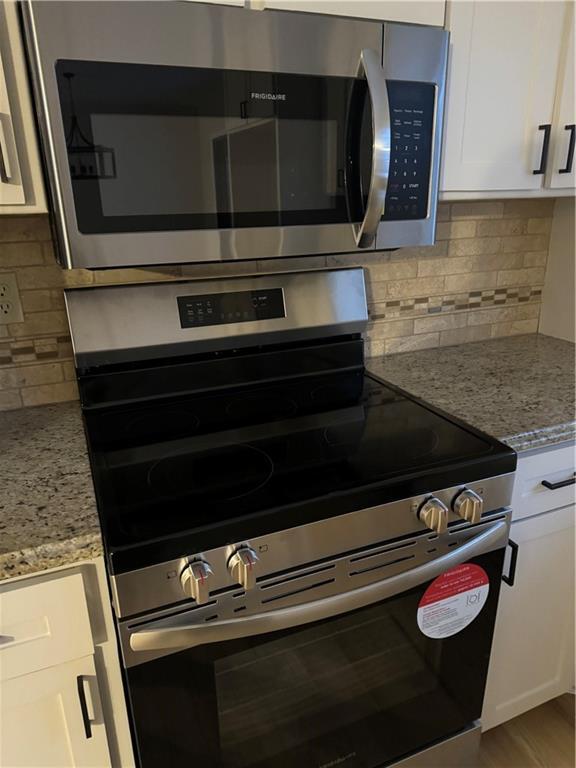 kitchen with hardwood / wood-style floors, white cabinetry, stainless steel appliances, light stone countertops, and decorative backsplash