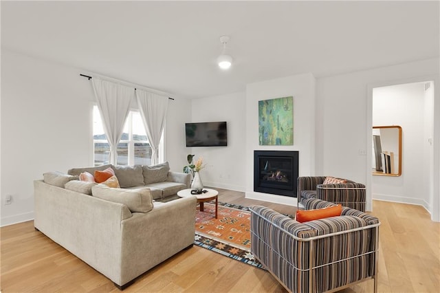 living room featuring a glass covered fireplace, light wood-style flooring, and baseboards