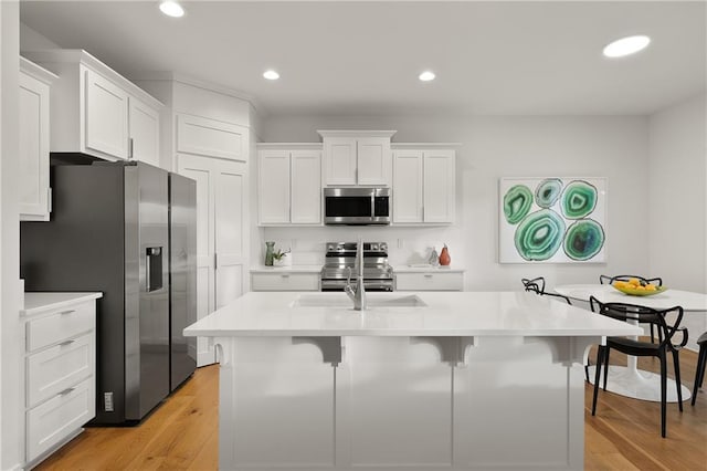 kitchen with white cabinets, light wood finished floors, a breakfast bar area, and stainless steel appliances