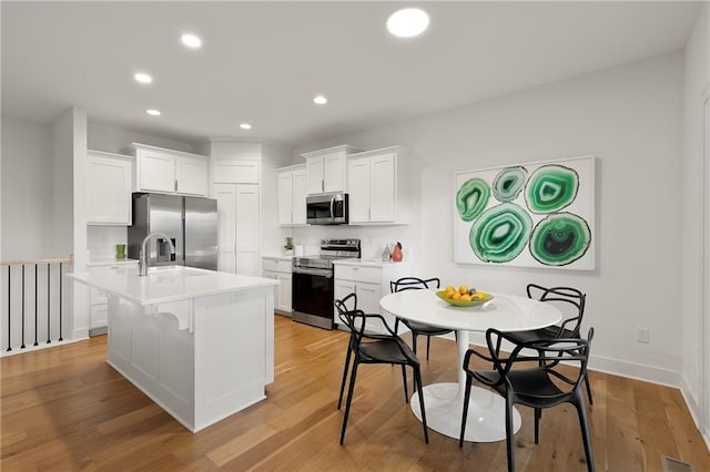 kitchen featuring a center island with sink, light countertops, appliances with stainless steel finishes, light wood-style floors, and white cabinetry