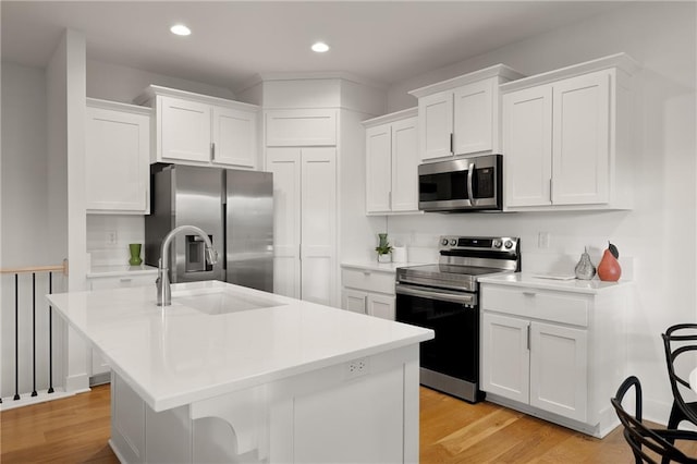 kitchen with appliances with stainless steel finishes, a kitchen island with sink, light countertops, white cabinetry, and a sink