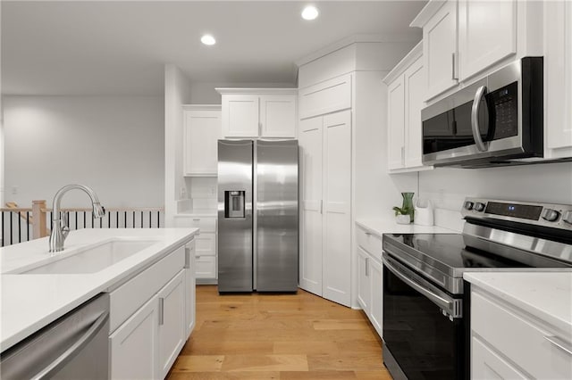 kitchen featuring white cabinets, light wood-style flooring, appliances with stainless steel finishes, light countertops, and a sink