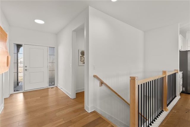 hall with light wood-style floors, baseboards, and an upstairs landing