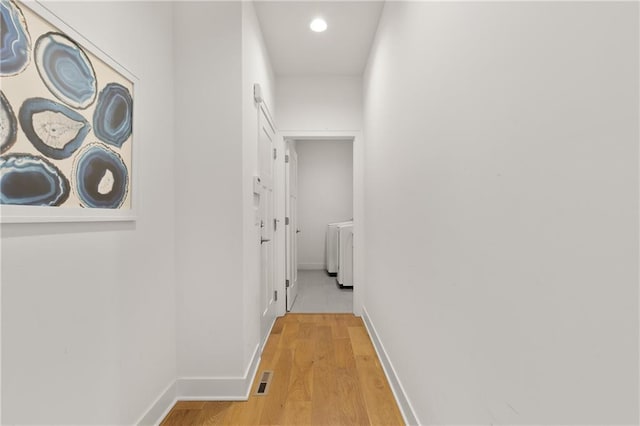 hallway with light wood-style floors, visible vents, and baseboards