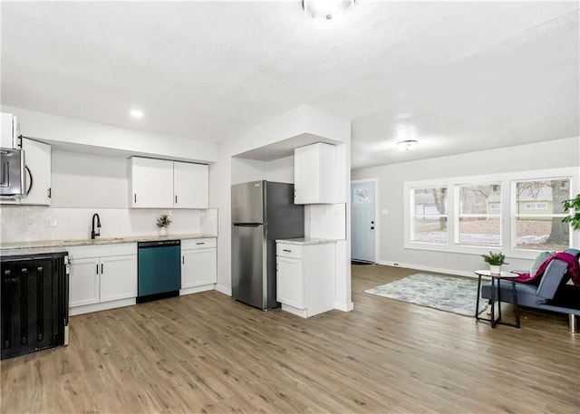 kitchen with appliances with stainless steel finishes, light hardwood / wood-style flooring, white cabinets, decorative backsplash, and sink