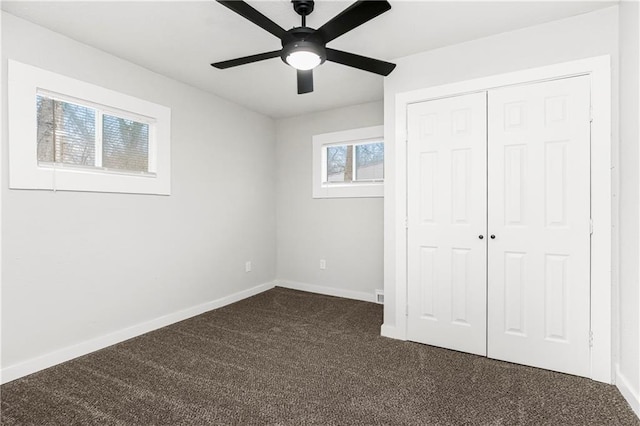 unfurnished bedroom with ceiling fan, dark colored carpet, and a closet