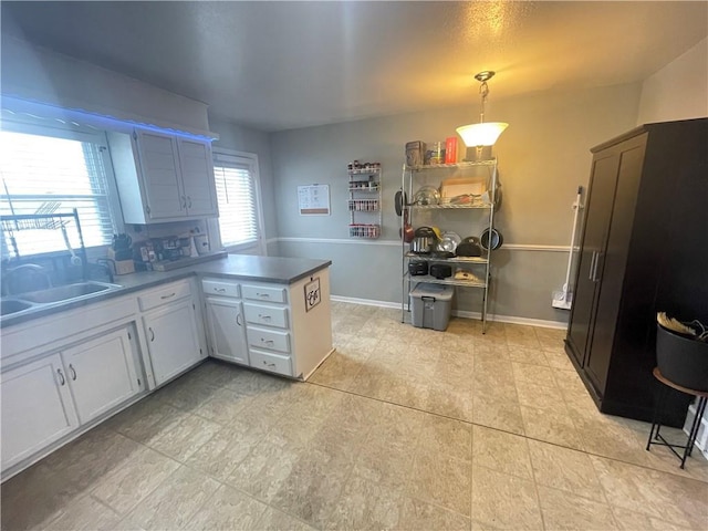 kitchen featuring pendant lighting, kitchen peninsula, sink, and white cabinets