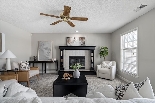 living room featuring ceiling fan, light colored carpet, a tiled fireplace, and a textured ceiling