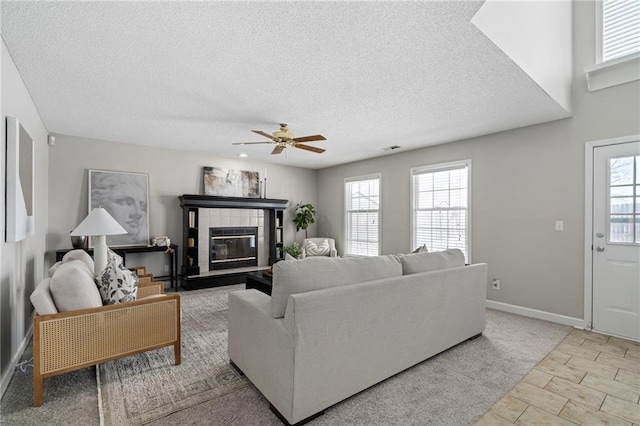 living room featuring a tile fireplace, ceiling fan, and a textured ceiling