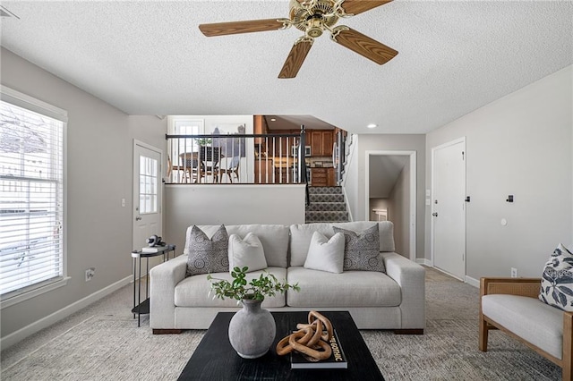 living room featuring ceiling fan, light colored carpet, and a textured ceiling