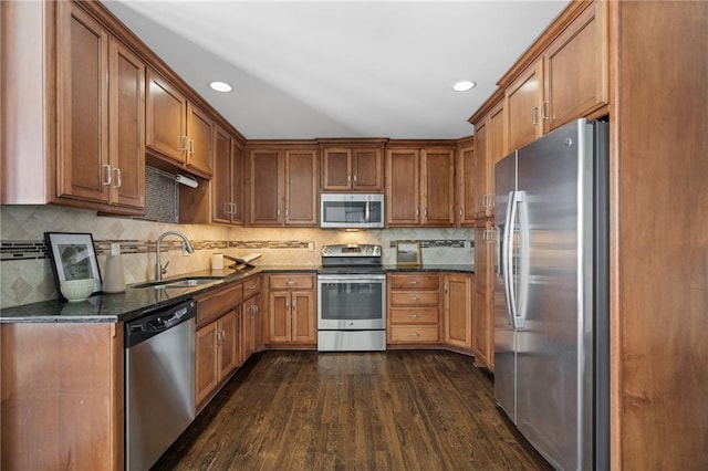 kitchen with dark wood-type flooring, sink, dark stone countertops, stainless steel appliances, and backsplash