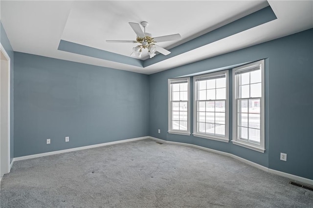 empty room featuring a raised ceiling, carpet flooring, and ceiling fan