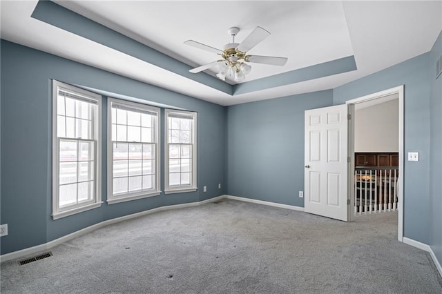 carpeted spare room featuring a raised ceiling and ceiling fan