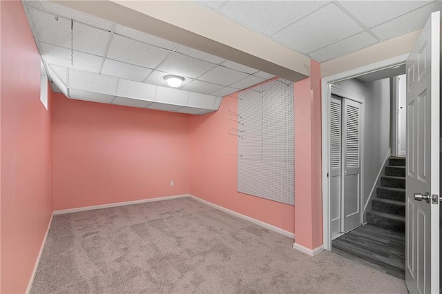 basement featuring a paneled ceiling and light colored carpet