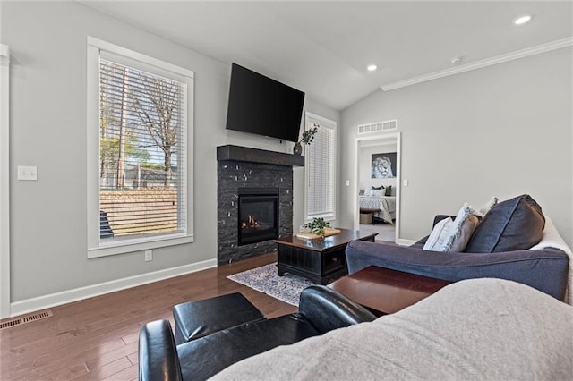 living area with lofted ceiling, wood finished floors, visible vents, baseboards, and a glass covered fireplace