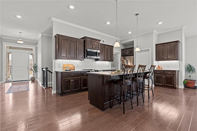 kitchen featuring dark wood-style flooring, appliances with stainless steel finishes, a kitchen breakfast bar, and dark brown cabinets