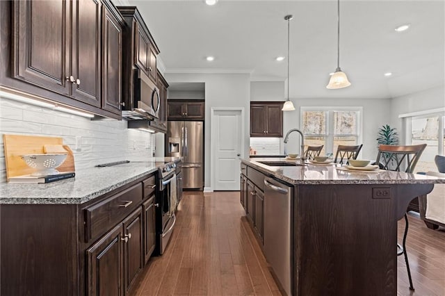 kitchen with dark brown cabinetry, dark wood-style floors, a kitchen breakfast bar, stainless steel appliances, and a sink