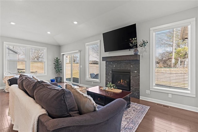 living room featuring a glass covered fireplace, wood-type flooring, visible vents, and baseboards