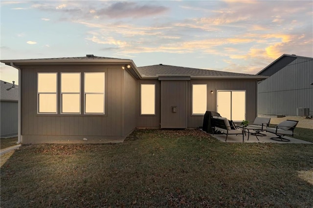 back of house at dusk featuring a patio and a lawn