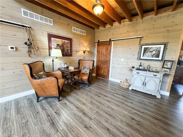 living area featuring a barn door, beam ceiling, visible vents, and wood finished floors