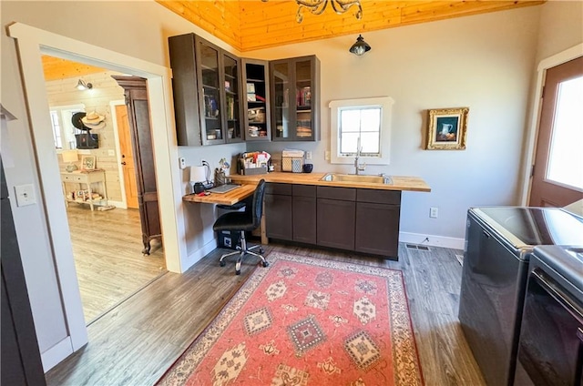 kitchen featuring glass insert cabinets, a sink, washer and clothes dryer, and wood finished floors